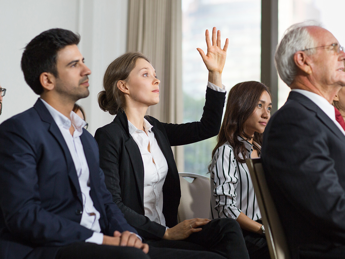 Audience member raising her hand to ask a question during a conference