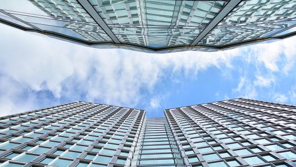 Modern glass skyscrapers seen from below against a blue sky with clouds