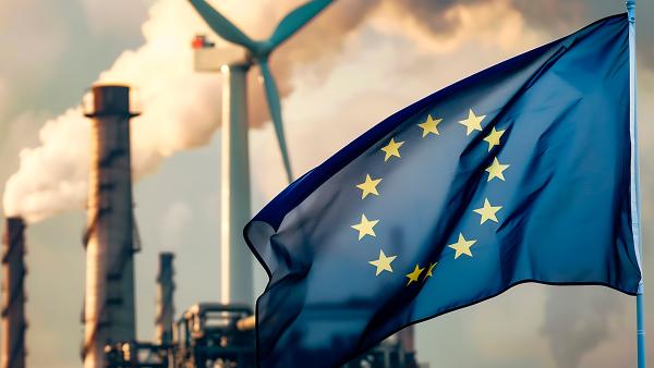 	European Union flag in front of an industrial plant with smoking chimneys and a wind turbine